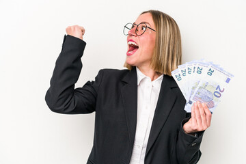 Young business caucasian woman holding banknotes isolated on white background raising fist after a victory, winner concept.