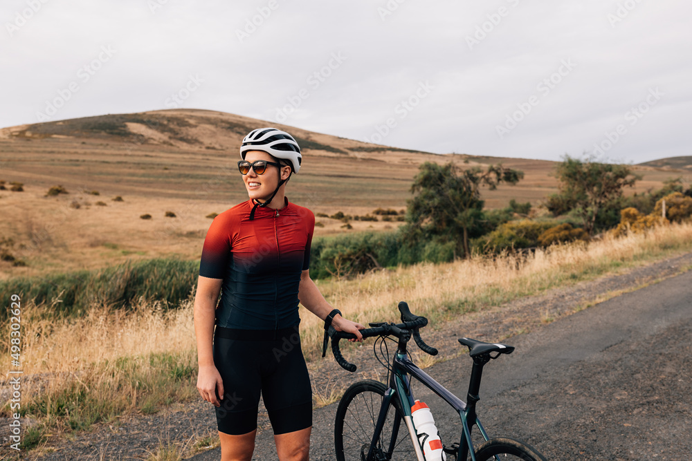 Wall mural Sportswoman wearing a cycling helmet and sunglasses standing with a bicycle on an empty road