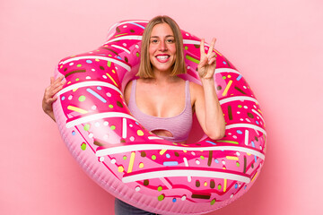 Obraz na płótnie Canvas Young caucasian woman holding an air mattress isolated on pink background showing number two with fingers.