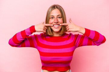 Young caucasian woman isolated on pink background smiles, pointing fingers at mouth.