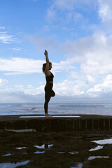 Young woman practice yoga on a beautiful beach at sunrise. Blue sky, ocean, waves, proximity to nature, unity with nature.
