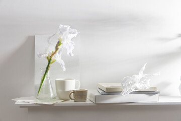 A vase with white iris, cup of different size, frame for photos, box and album on the table. Scandinavian style.