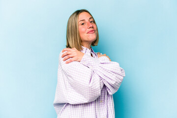 Young caucasian woman isolated on blue background hugs, smiling carefree and happy.