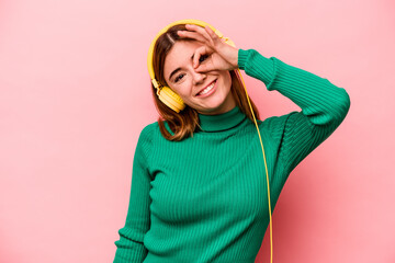 Young caucasian woman listening to music isolated on pink background excited keeping ok gesture on eye.