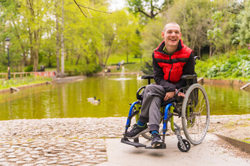 A person with a disability in a public park in the city. Sitting in the wheelchair - obrazy, fototapety, plakaty