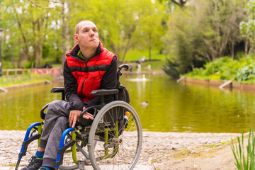 Fototapeta na wymiar Portrait of a paralyzed young man in a public park in the city. Sitting in the wheelchair thoughtful