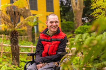 Fototapeta na wymiar Portrait of a person with a disability in a public park in the city. Sitting in the wheelchair smiling