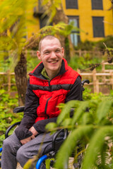 Portrait of a person with a disability in a red vest in a public park in the city. Sitting in the wheelchair smiling