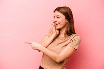 Young caucasian woman isolated on pink background saying a gossip, pointing to side reporting something.