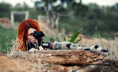 Sniper girl in a green field. Military snipers. The sniper smokes. Red-haired girl in camouflage....