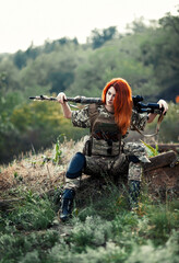 Sniper girl in a green field. Military snipers. The sniper smokes. Red-haired girl in camouflage. Fighting

