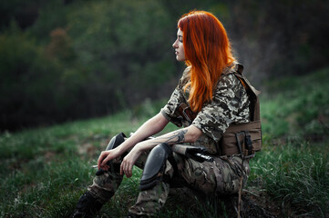 Sniper girl in a green field. Military snipers. The sniper smokes. Red-haired girl in camouflage. Fighting
