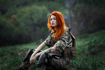 Fototapeta na wymiar Sniper girl in a green field. Military snipers. The sniper smokes. Red-haired girl in camouflage. Fighting 