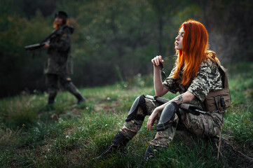 Sniper girl in a green field. Military snipers. The sniper smokes. Red-haired girl in camouflage. Fighting

