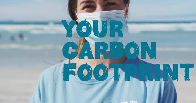 Animation of your carbon footprint text in blue over caucasian woman in face mask on beach