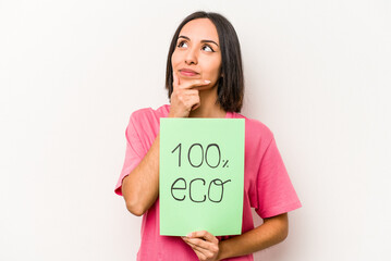 Fototapeta na wymiar Young hispanic woman holding 100% eco placard isolated on white background looking sideways with doubtful and skeptical expression.