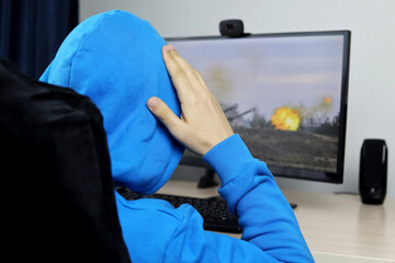 Man in hoodie sitting at desktop PC and looking at the firing artillery. Video news about the war...