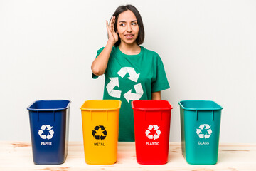 Young hispanic woman recycling isolated on white background trying to listening a gossip.