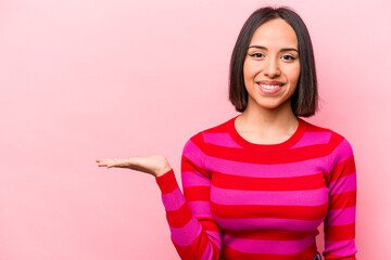 Young hispanic woman isolated on pink background showing a copy space on a palm and holding another...