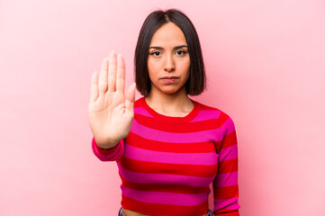 Young hispanic woman isolated on pink background standing with outstretched hand showing stop sign,...