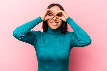 Young hispanic woman isolated on pink background showing okay sign over eyes