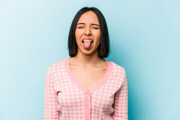 Fototapeta premium Young hispanic woman isolated on blue background funny and friendly sticking out tongue.