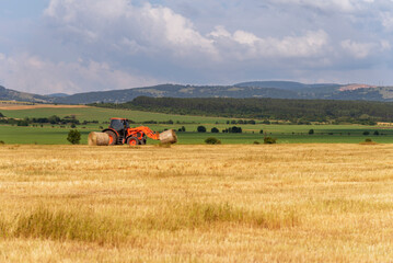 Tractor lifting hay bale on barrow.