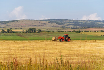 Obraz premium Tractor lifting hay bale on barrow.