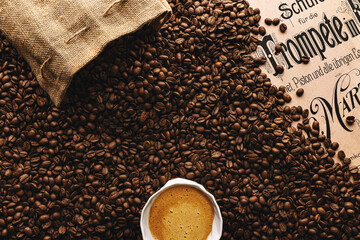 Naklejka premium A white cup of coffee with foam in a sea of coffee beans coming out of a cloth bag and partially covering a vintage trumpet playing method book