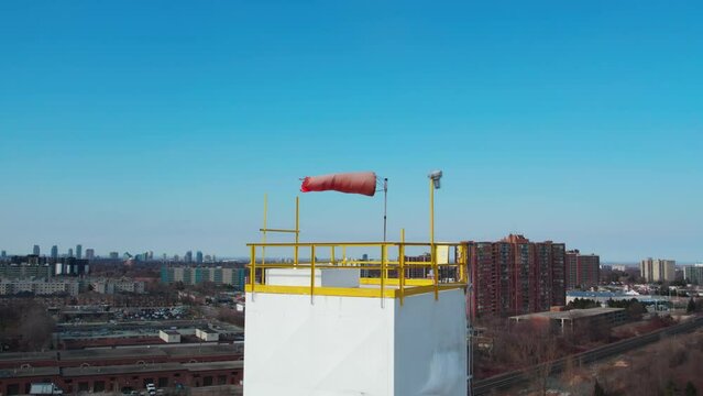 Windsock with blue sky and city in the background. Slow motion of conical tube flag for wind direction and speed. Used in airports and manufacturing facilities. Aerial.