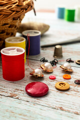 vertical take of elements for sewing such as spools of thread of different colors in focus and a wicker sewing box and various buttons. Out of focus background