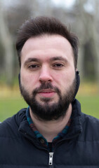 Fototapeta premium Portrait of man with earmuff. No expression on his face. Outdoor background. Close up photo. 