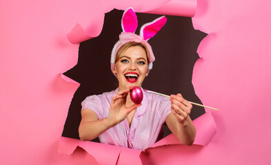 Happy Woman in fake bunny ears painting easter egg. Rabbit girl with paint brush and pink egg.