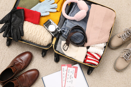Open suitcase with warm clothes, accessories and shoes on floor, flat lay