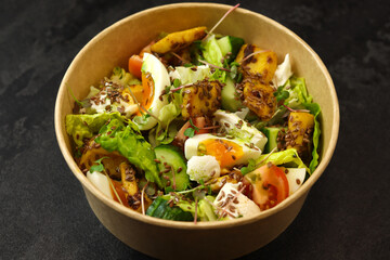 Healthy bowl with fried squid, egg, tomatoes, cucumbers, lettuce, cream cheese and flax seeds salad isolated on dark background. Food delivery service and daily ration concept.