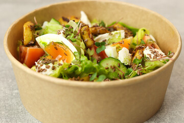 Healthy bowl with fried squid, egg, tomatoes, cucumbers, lettuce, cream cheese and flax seeds salad isolated on gray background. Food delivery service and daily ration concept.