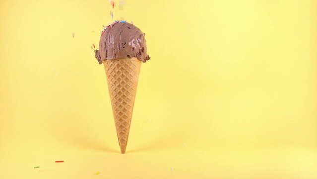 funny creative concept of wafer cone with ice cream covered and strewing sprinkles on yellow background, copy space, slow motion, cinemagraph