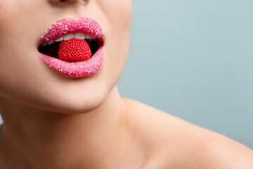 Woman with lips covered in sugar eating candy on light grey background, closeup. Space for text