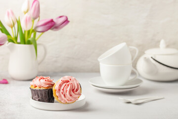 Cupcakes, tulips and white utensils for a tea ceremony on a bright background. Holiday concept
