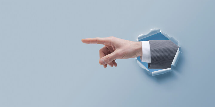 Businessman Hand Pointing Through A Hole In Paper