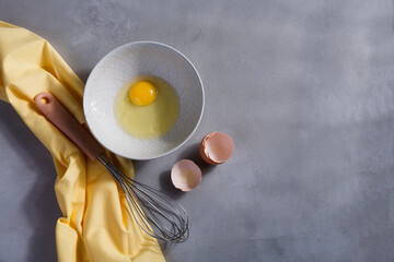 A bowl with yolk and a whisk on gray kitchen table with yellow cloth, copy space