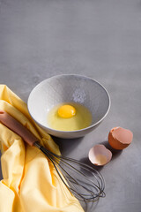 A bowl with yolk and a whisk on gray kitchen table with yellow cloth, copy space