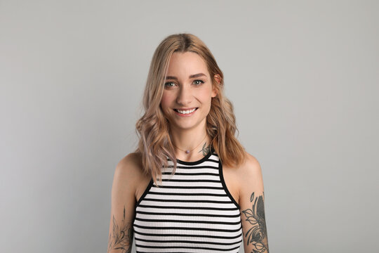 Beautiful woman with tattoos on body against grey background