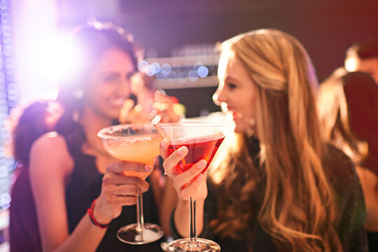 Clink before you drink. Shot of two young women drinking cocktails at a party.