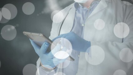 Animation of light spots over caucasian male doctor with tablet and face mask - Powered by Adobe