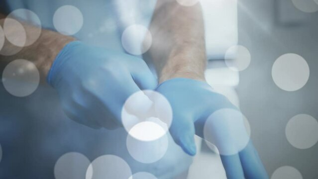 Animation Of Light Spots Over Caucasian Male Doctor Wearing Medical Gloves