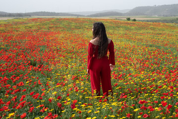 Young woman dressed on red standing in the blooming field in spring