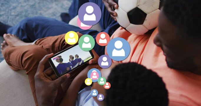 Animation of social media icons over african american father and son watching football on smartphone