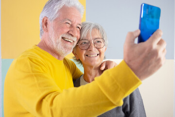 Happy caucasian beautiful senior couple standing over isolated colorfed background video calling with smart phone. Elderly white-haired people smiling carefree enjoying retirement