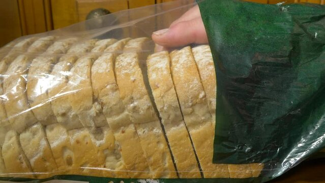 Closeup of a man's hand taking slices of white bread with grains, from a retail packet.